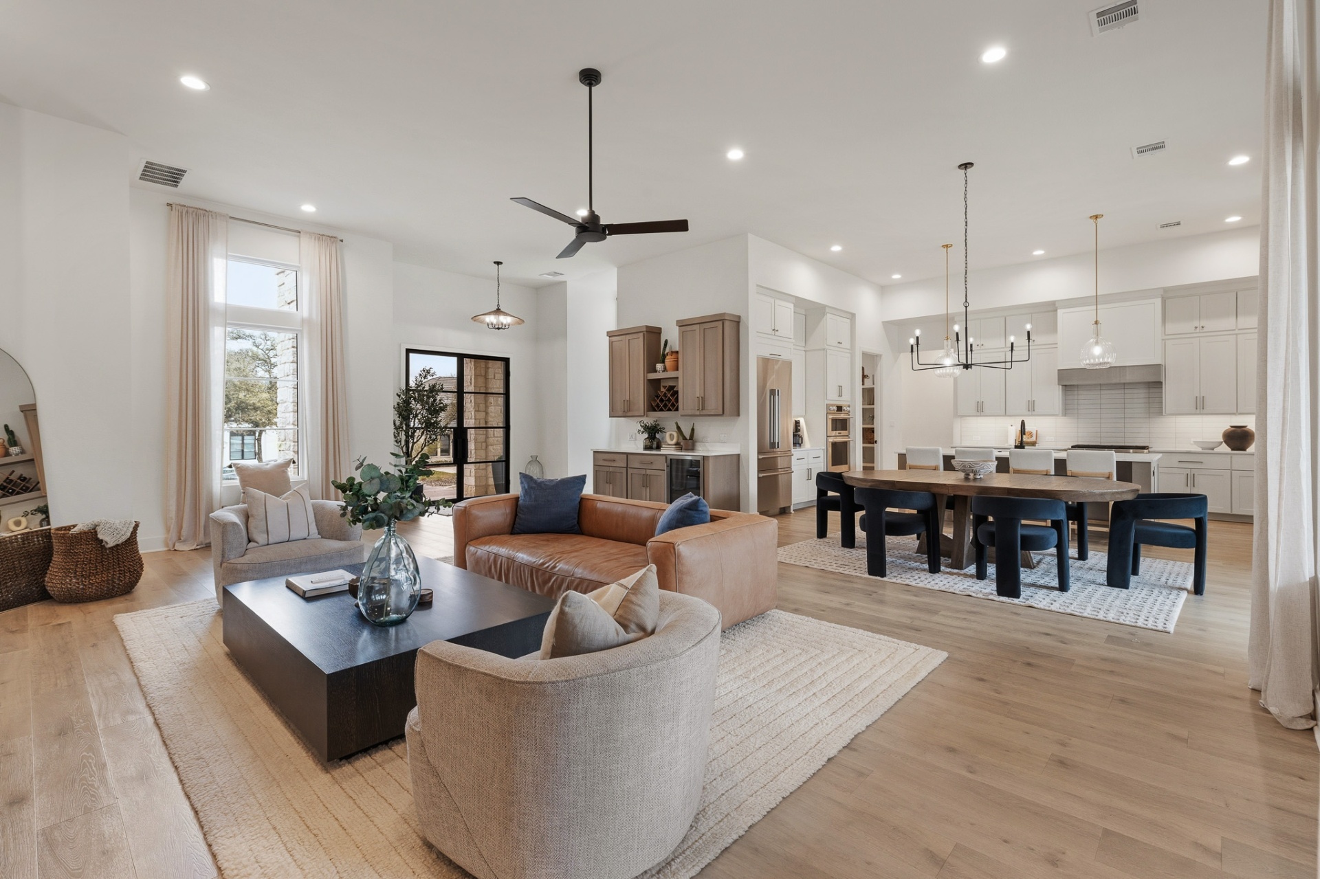 Open-concept living, dining and kitchen with soaring ceilings, leather sofa, round dining table and black steel entry door