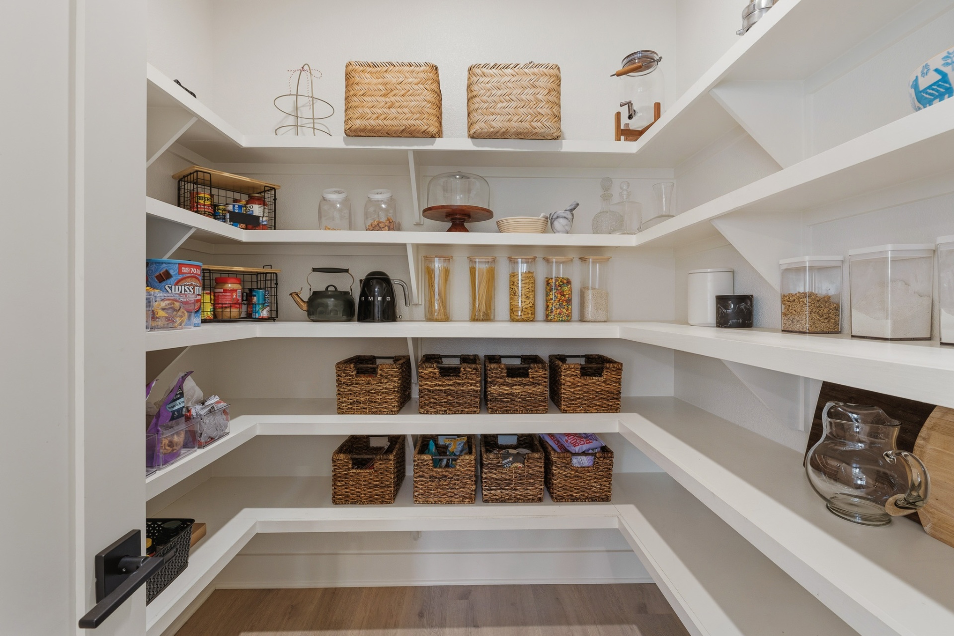 Walk-in pantry with white built-in shelving, woven baskets and abundant storage
